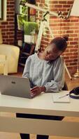 Vertical video Freelancer writing information from phone call discussion at sunset, working remotely overtime and answering calls. African american person taking notes of telephone conversation.