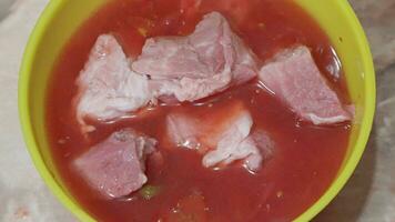 Pieces of pork meat are dipped in tomato sauce for marinating. video
