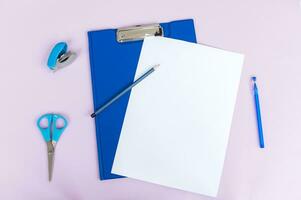 Clipboard with a white sheet and a pen highlighted on a light background. Top view photo