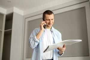A cheerful man looks at an album and makes a call on the phone. Indoor repair work photo