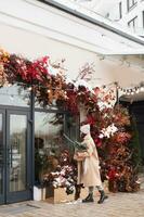 A stylish young woman with branches of nobilis looks into the windows of Christmas shops photo