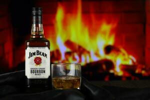 KYIV, UKRAINE - MAY 4, 2022 Jim Beam original alcohol bottle on wooden table with red fireplace photo