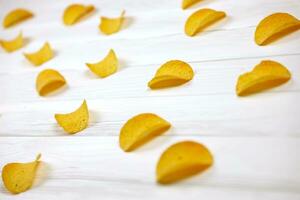 Many orange Pringles potato snack chips on white wooden table. Pringles is a brand of potato snack chips owned by Kellogg Company photo