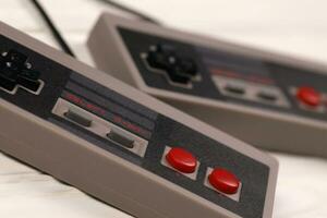 KHARKOV, UKRAINE - DECEMBER 27, 2020 Two old gamepads for 8-bit video game consoles nintendo entertainment system and nes mini on white table. Old school retro gaming photo