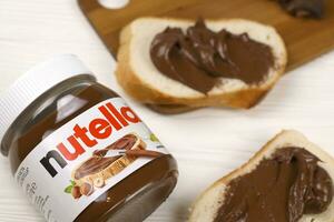 kharkov, ucrania - 27 de diciembre de 2020 lata de vidrio de nutella y untada en pan recién horneado. nutella es fabricada por la empresa italiana ferrero introducida por primera vez en 1964 foto