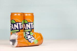 KHARKOV, UKRAINE - DECEMBER 8, 2020 Aluminium cans of Fanta soft drink on white wooden table. Fanta is brand of carbonated soft drinks created by The Coca-Cola Company in 1940 photo