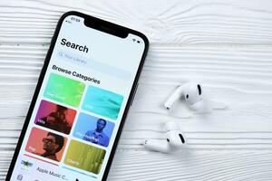 KHARKOV, UKRAINE - MARCH 5, 2021 Apple music icon and application from App store on iPhone 12 pro display screen with airpods pro on white table photo