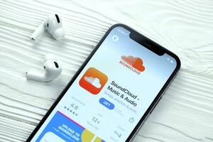 KHARKOV, UKRAINE - MARCH 5, 2021 Soundcloud icon and application from App store on iPhone 12 pro display screen with airpods pro on white table photo