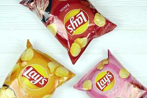 KHARKOV, UKRAINE - JANUARY 3, 2021 Various flavoured of lay's potato chips on wooden background. Lay's has been owned by PepsiCo through Frito-Lay in 1965 photo