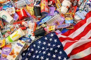 KHARKOV, UKRAINE - AUGUST 10, 2021 US flag on big pile of various wrappings and empty disposable packages and cups from famous branded food production photo