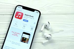KHARKOV, UKRAINE - MARCH 5, 2021 Apple music icon and application from App store on iPhone 12 pro display screen with airpods pro on white table photo