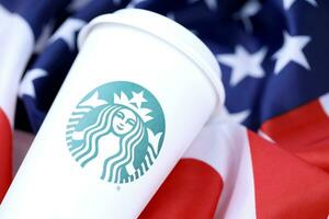 KHARKOV, UKRAINE - MARCH 15, 2021 Starbucks cup on US flag. Starbucks Corporation is multinational chain of coffeehouses headquartered in Seattle, Washington photo