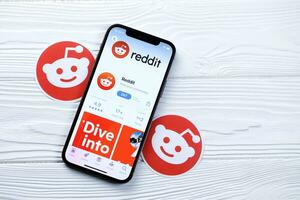 KHARKOV, UKRAINE - MARCH 5, 2021 Reddit icon and application from App store on iPhone 12 pro display screen on white table photo