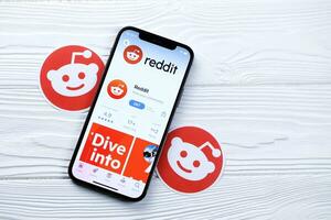 KHARKOV, UKRAINE - MARCH 5, 2021 Reddit icon and application from App store on iPhone 12 pro display screen on white table photo