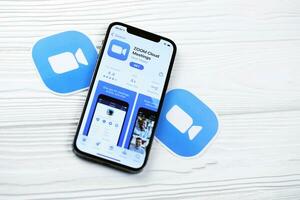 KHARKOV, UKRAINE - MARCH 5, 2021 Zoom messenger icon and application from App store on iPhone 12 pro display screen on white table photo