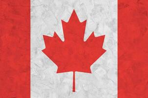 Canada flag depicted in bright paint colors on old relief plastering wall. Textured banner on rough background photo