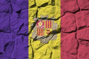 Andorra flag depicted in paint colors on old stone wall closeup. Textured banner on rock wall background photo