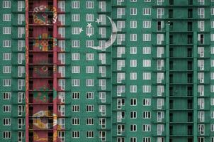 Turkmenistan flag depicted in paint colors on multi-storey residental building under construction. Textured banner on brick wall background photo