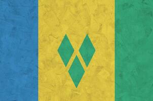Saint Vincent and the Grenadines flag depicted in bright paint colors on old relief plastering wall. Textured banner on rough background photo