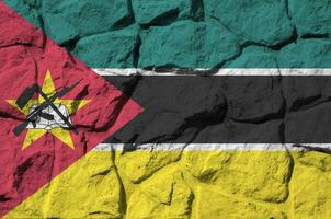 Mozambique flag depicted in paint colors on old stone wall closeup. Textured banner on rock wall background photo