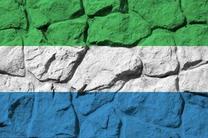 Sierra Leone flag depicted in paint colors on old stone wall closeup. Textured banner on rock wall background photo