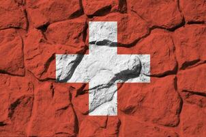 Switzerland flag depicted in paint colors on old stone wall closeup. Textured banner on rock wall background photo