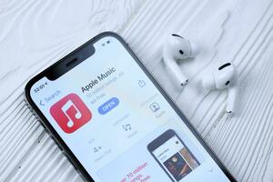 KHARKOV, UKRAINE - MARCH 5, 2021 Apple music icon and application from App store on iPhone 12 pro display screen with airpods pro on white table photo