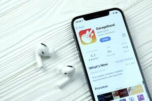 KHARKOV, UKRAINE - MARCH 5, 2021 Garageband for artists icon and application from App store on iPhone 12 pro display screen with airpods pro on white table photo