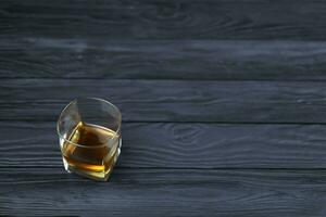 Glass with cognac or whisky alcohol drink on black wooden table close up with copy space for text. Elite alcohol drinking or alcoholism concept photo