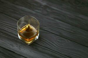 Glass with cognac or whisky alcohol drink on black wooden table close up with copy space for text. Elite alcohol drinking or alcoholism concept photo