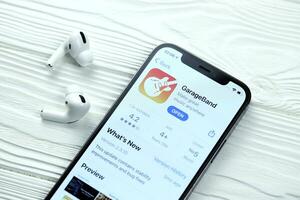 KHARKOV, UKRAINE - MARCH 5, 2021 Garageband for artists icon and application from App store on iPhone 12 pro display screen with airpods pro on white table photo