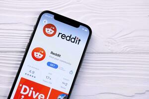 KHARKOV, UKRAINE - MARCH 5, 2021 Reddit icon and application from App store on iPhone 12 pro display screen on white table photo
