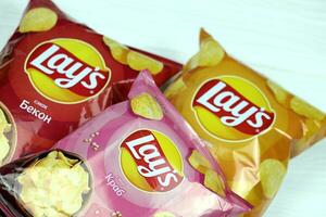 KHARKOV, UKRAINE - JANUARY 3, 2021 Various flavoured of lay's potato chips on wooden background. Lay's has been owned by PepsiCo through Frito-Lay in 1965 photo