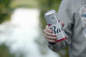 Can of Budweiser Bud beer in male hand on a river and green trees blurred background photo