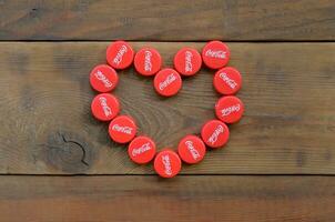 Heart of many red caps with coca cola logo on wooden background photo