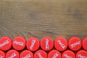 Many red caps with coca cola logo on wooden background photo