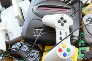 Pile of old 8-bit video game consoles and many gaming accessories like a joysticks and cartridges photo