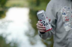 Can of Budweiser Bud beer in male hand on a river and green trees blurred background photo