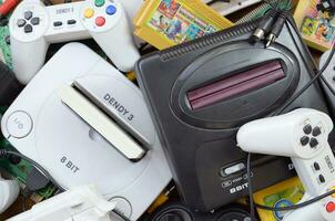 Pile of old 8-bit video game consoles and many gaming accessories like a joysticks and cartridges photo