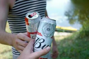 Young man raise Budweiser Bud beer can with male friend on blurred river with kayak and trees photo