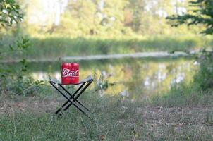 Budweiser Bud beer cans pack on folding chair outdoors at the river and green trees background photo