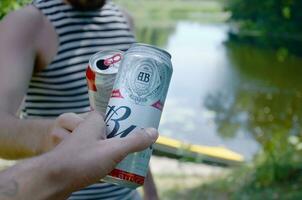 Young man raise Budweiser Bud beer can with male friend on blurred river with kayak and trees photo