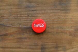 Single red bottle lid with Coca Cola logo on wooden background photo