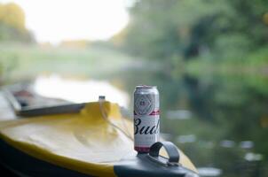 Budweiser Bud beer can on yellow kayak outdoors in the river and green trees blurred background photo