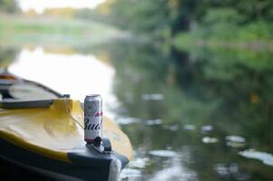 Budweiser Bud beer can on yellow kayak outdoors in the river and green trees blurred background photo