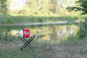 Budweiser Bud beer cans pack on folding chair outdoors at the river and green trees background photo