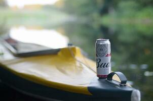 Budweiser Bud beer can on yellow kayak outdoors in the river and green trees blurred background photo