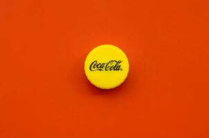 Single yellow bottle lid with Coca Cola logo on red background photo
