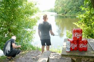 Budweiser Bud beer cans pack on old table and fisherman at river on background photo