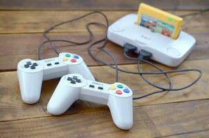 Old 8-bit video game console with game cartridge and two gaming joysticks on wooden background photo